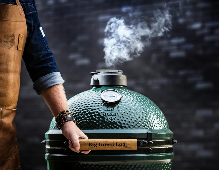 Persona abriendo un Big Green Egg del que sale humo