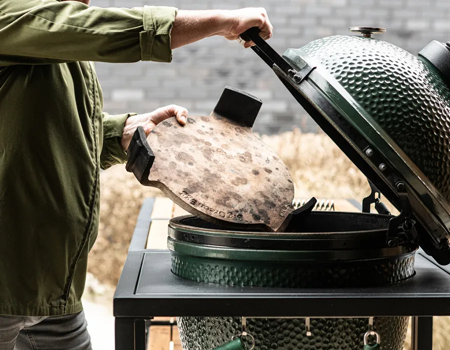 Persona colocando una piedra en un Big Green Egg abierto